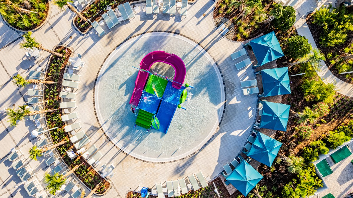 Top-down aerial of the splash pad ringed by blue umbrellas in Clermont