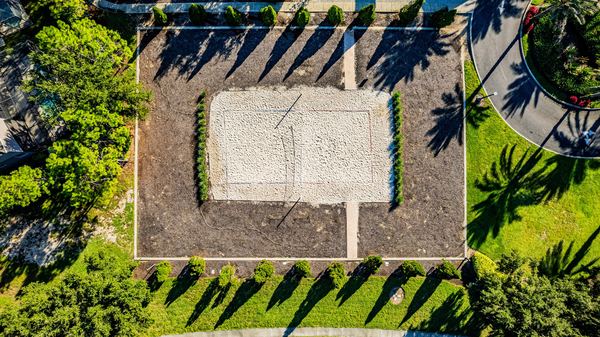Top-down aerial of a sand volleyball court framed by palm shadows in Four Corners