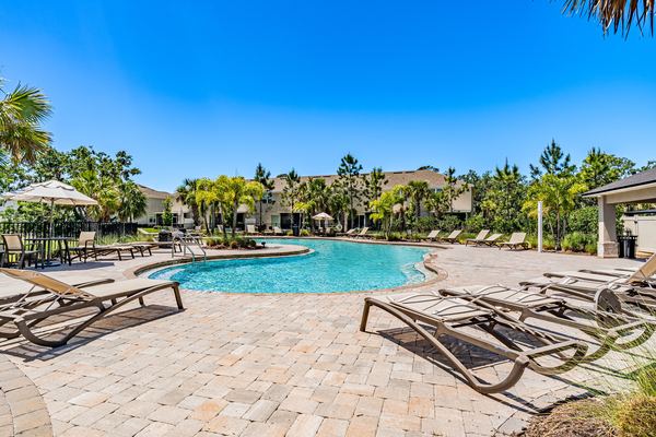 Curved resort pool with a stone deck, empty loungers and a closed umbrella, the clubhouse and palms behind in Palmetto