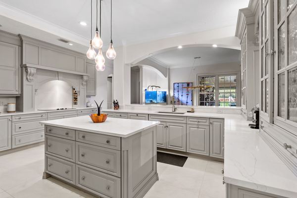 Grey cabinet kitchen with a white marble island, three glass pendant lights and an arched marble alcove over the cooktop; an aquarium sits in the room beyond the pass-through.