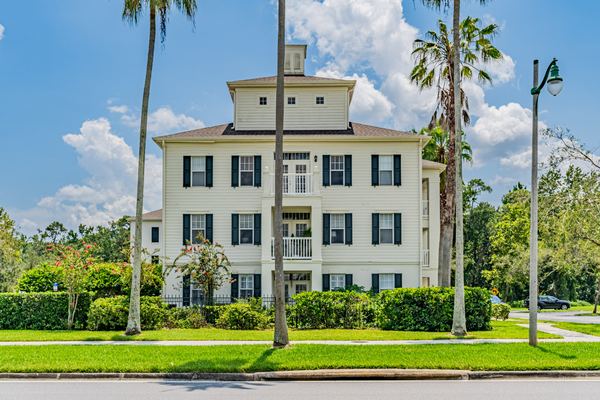Three-story pale yellow classical home with black shutters and tall palms in Celebration