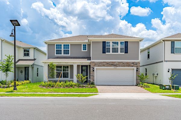Two-storey home in taupe siding with navy shutters, a stone-clad garage wall, a covered entry porch and a paver driveway.