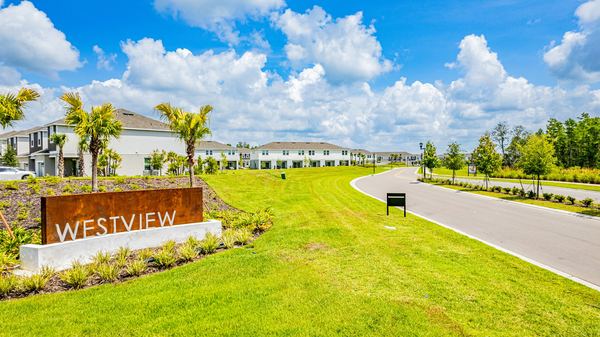 Community entrance sign beside a road with apartment buildings behind in Poinciana