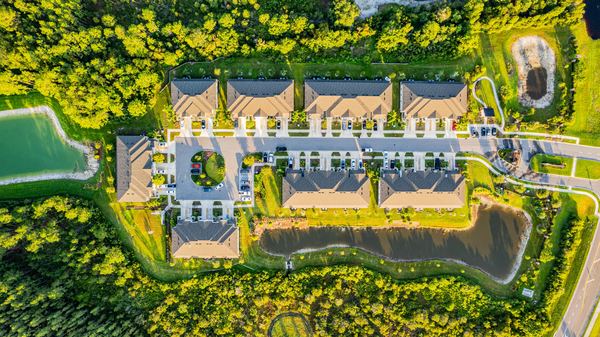 Top-down aerial of townhome rows beside a retention pond in Wesley Chapel
