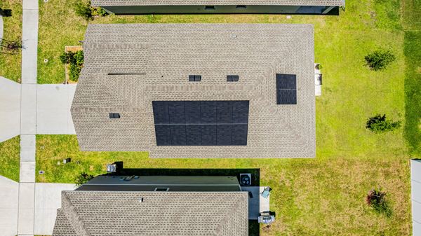 Straight-down aerial of a single-storey roof carrying two solar arrays, with neighbouring roofs and lawn on either side.