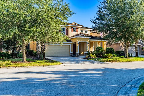 Tan two-story home with a three-car garage behind mature oaks in Four Corners
