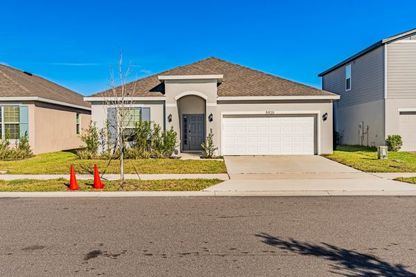 Tan single-story new-build home with traffic cones on the unfinished lot in Haines City