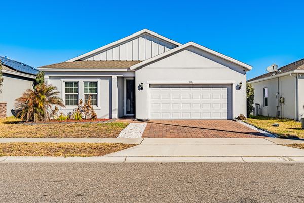 White single-story home with a paver driveway and a young palm in Haines City