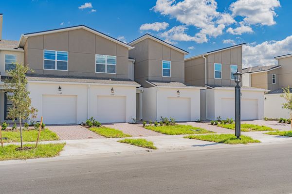 Row of attached two-storey townhomes with taupe upper storeys and white garage bays, each with its own paver walk to the street.