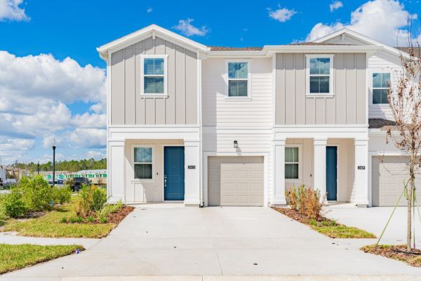 Two attached two-storey townhomes in white board-and-batten siding, with teal front doors and single garages on a shared concrete drive.