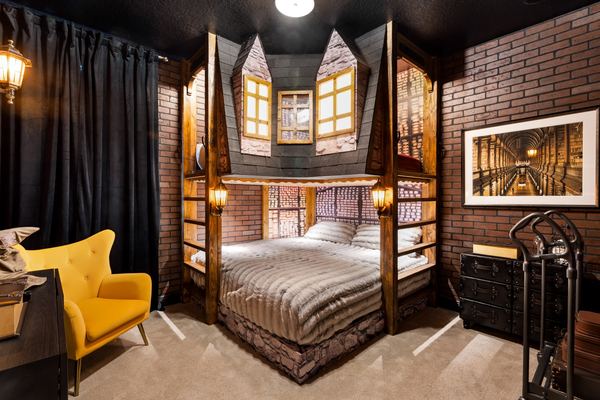 Themed bedroom built as a storefront facade around the bed, with brick walls, lantern sconces, a yellow armchair and a trunk-style dresser.