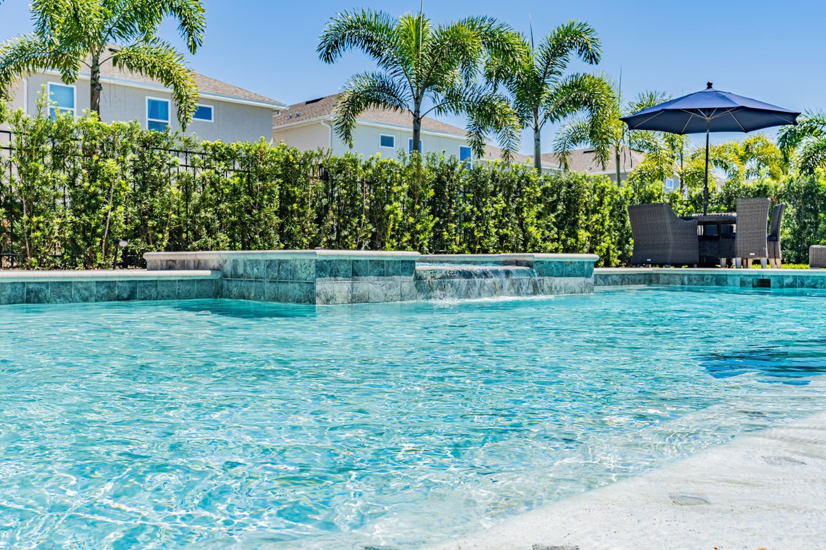 Freeform pool with a spa spillover behind a tall hedge in Kissimmee