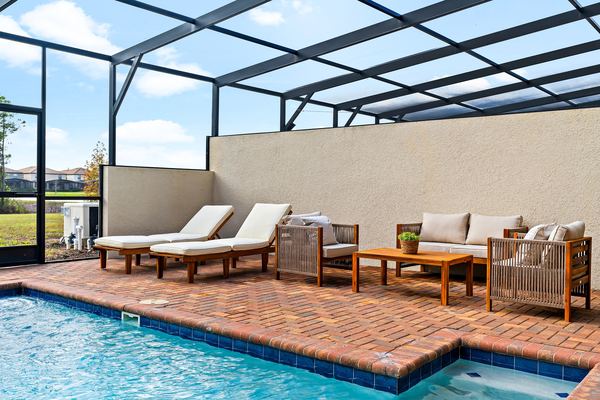 Screened lanai with a rectangular turquoise pool, a brick deck, two white loungers and wood outdoor sofas in Kissimmee