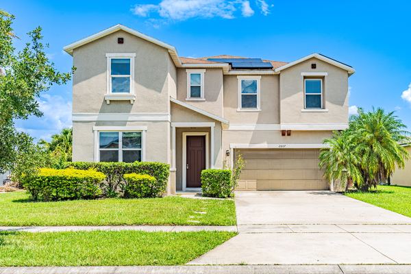 Two-story tan home with a roof solar panel and palms in Kissimmee