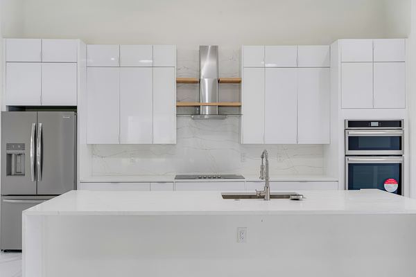 New white kitchen with flat-panel cabinets, a marble slab backsplash, a stainless chimney hood between two wood shelves and a waterfall quartz island.