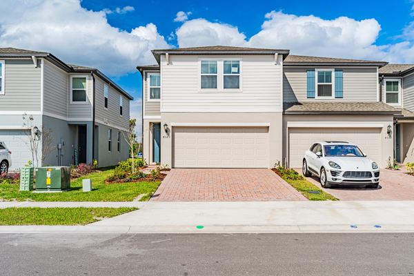 Cream two-story home with a paver driveway and a white SUV in St. Cloud