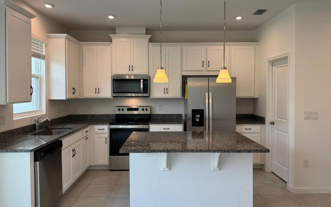 Kitchen with a granite island, two pendant lights and stainless appliances, photographed on a phone.